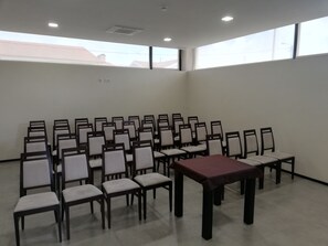 A conference room with rows of chairs and a table, large windows, and a ceiling light.