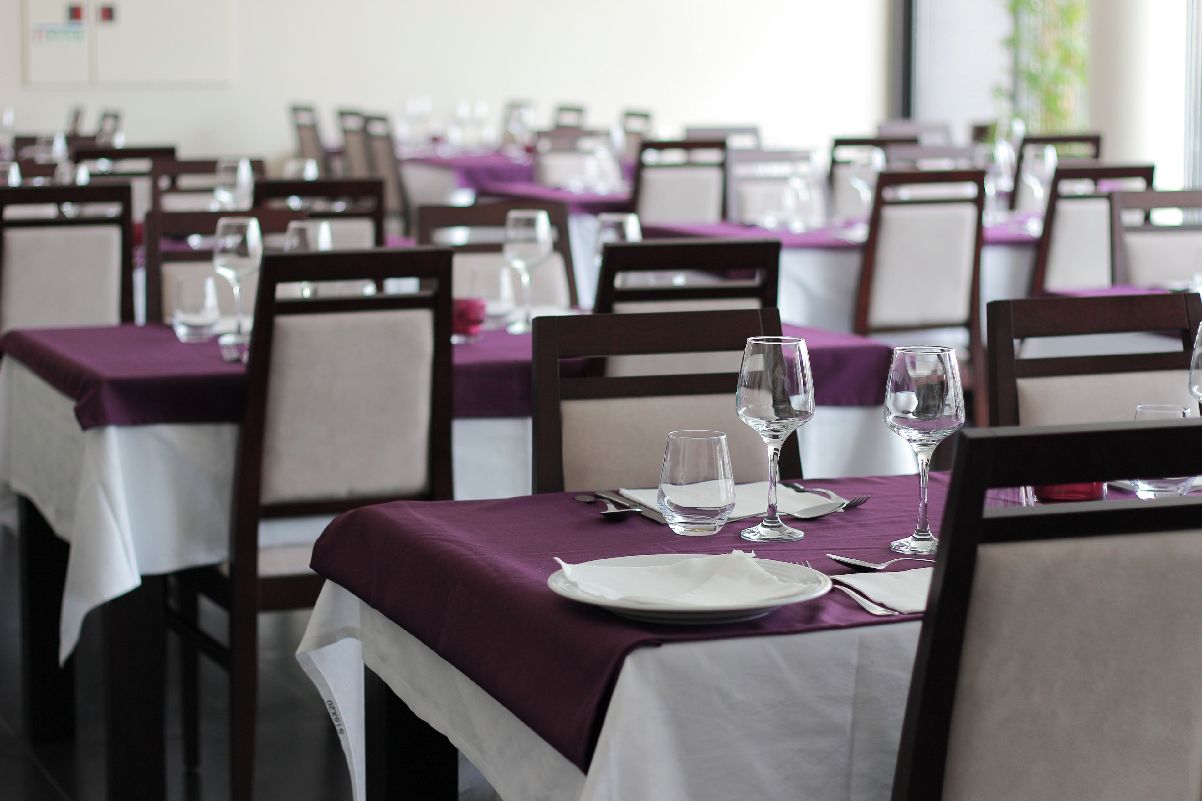Un restaurante con mesas dispuestas para comer, con manteles morados y vajilla blanca.