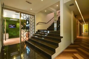 A modern staircase with a glass railing, leading to a room with a green accent wall and a flat-screen TV. - Laman Green The Boutique Hotel (Shah Alam)