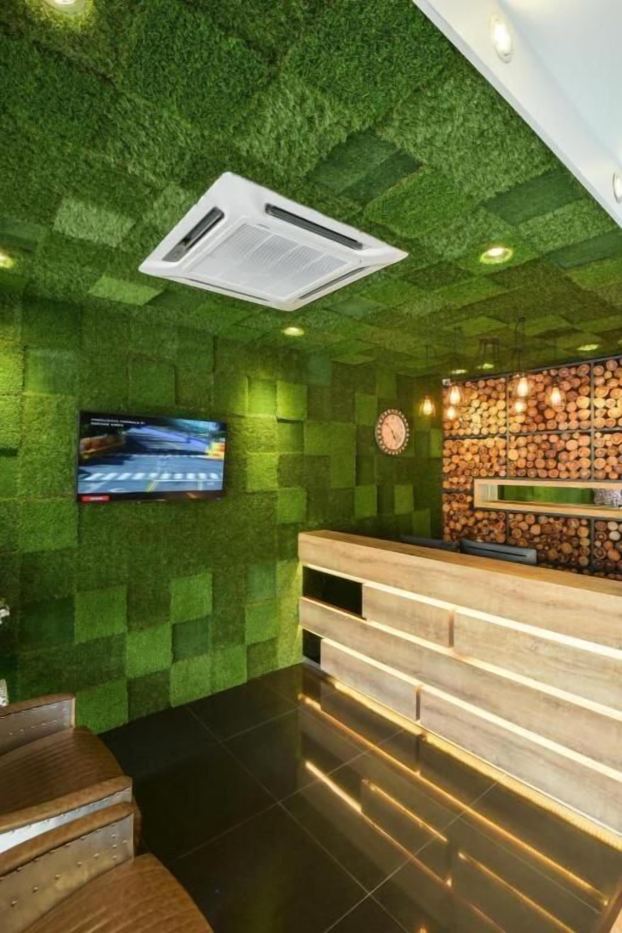 Un espace d’accueil avec un mur texturé de couleur verte, un comptoir d’accueil en bois, une horloge et un téléviseur fixé au mur.
