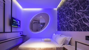 Una habitación de hotel moderna con una cama, un escritorio pequeño, un espejo y un televisor montado en la pared que muestra la temperatura ambiente.