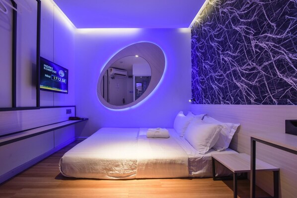 A modern hotel room with a bed, a small desk, a mirror, and a wall-mounted TV displaying room temperature. - Laman Green The Boutique Hotel (Shah Alam)