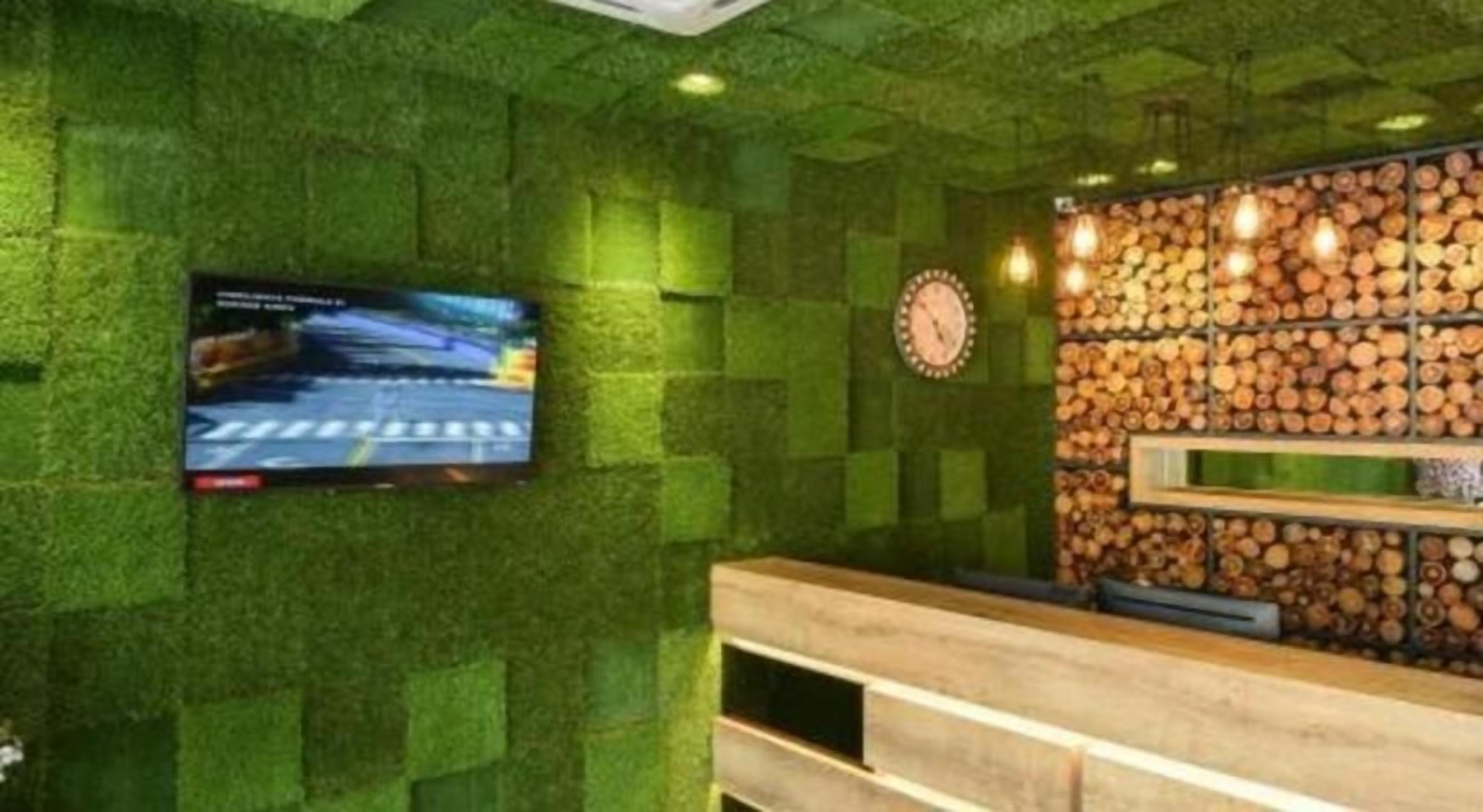 Ein Empfangsbereich mit grüner Wand mit Struktur, einem Wandfernseher, einer Uhr und einer Holzstoßwand.