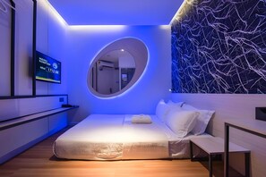 A modern bedroom with a bed, a round mirror, a TV, and a wall with a crackled pattern. - Laman Green The Boutique Hotel (Shah Alam)