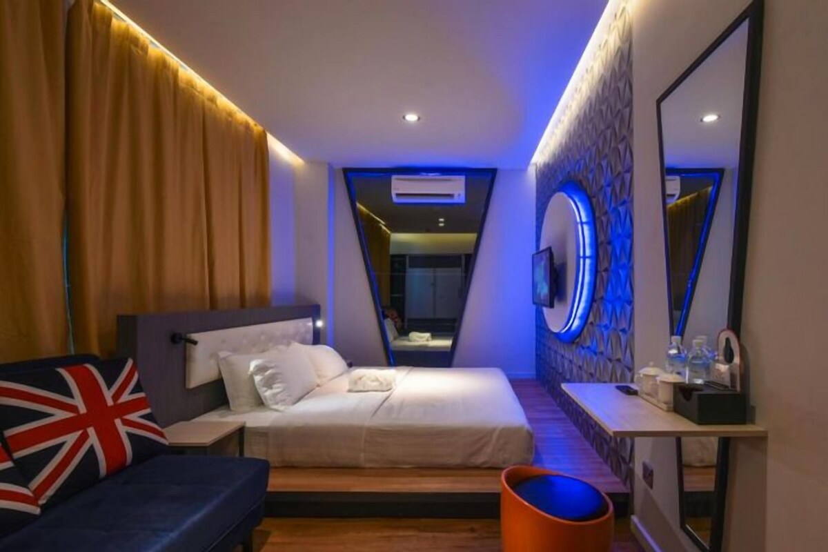 Una habitación de hotel moderna con cama, sofá, espejo y una mesita.