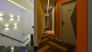 Un pasillo moderno de hotel con piso de diseño en patrón espiga, una escalera con barandilla de metal y una puerta con el número 215.
