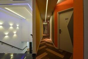 A modern hotel hallway with a herringbone-patterned floor, a staircase with a metal handrail, and a door labeled "215". - Laman Green The Boutique Hotel (Shah Alam)