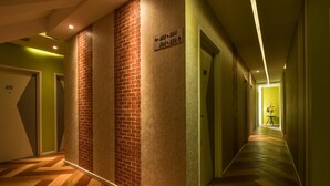Un pasillo de hotel con una pared de acento de ladrillo, un cartel con los números de las habitaciones y un suelo de madera con dibujo de espiga.