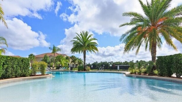 A large, clear swimming pool surrounded by palm trees and greenery, with a building in the background. - Oakwater, 3 bedrooms - The nearest resort from Disney! (Kissimmee)