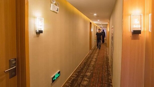 Passadís d'hotel amb portes de fusta, aplics de llum penjats a la paret i un sòl amb moqueta.