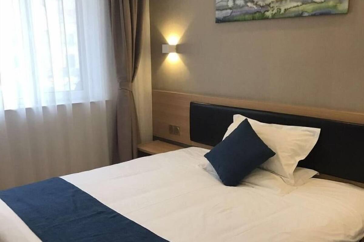 A hotel room with a bed, a painting on the wall, and a window with curtains.