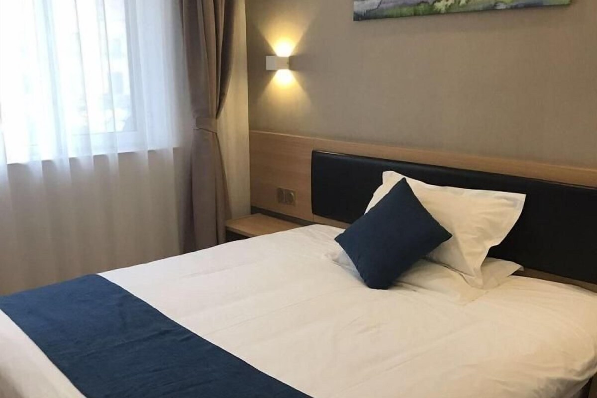 A hotel room with a bed, a painting on the wall, and a window with curtains.