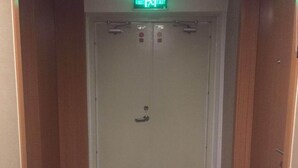 Una porta d'ascensor tancada, amb un extintor a l'esquerra i un senyal de sortida verd a la part superior.