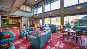 A spacious lobby with a red floral carpet, multiple seating areas including sofas and chairs, large windows offering views of the outdoors, and a reception desk. - Hotel Hanaya (Achi)