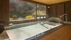 A hot tub in a room with large windows, wooden walls, and a tiled floor. - Hotel Hanaya (Achi)