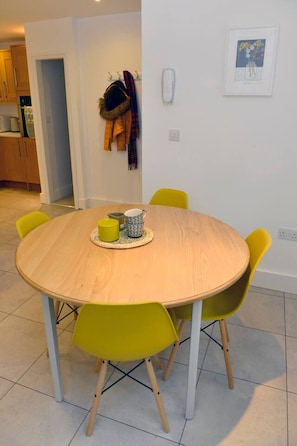 A round wooden dining table with four yellow chairs, a small yellow mug, and a patterned cup on a woven placemat. - Ruston Chambers Free parking, luxury 2 bedroom (Saint Ives)