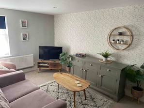 A living room with a sofa, a coffee table, a TV, a cabinet, and a wall with a circular shelf. - Ruston Chambers Free parking, luxury 2 bedroom (Saint Ives)
