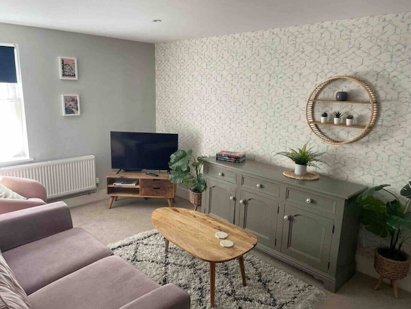 Un salon comprenant un canapé, une table basse, un téléviseur, un meuble et un mur orné d’une étagère circulaire.