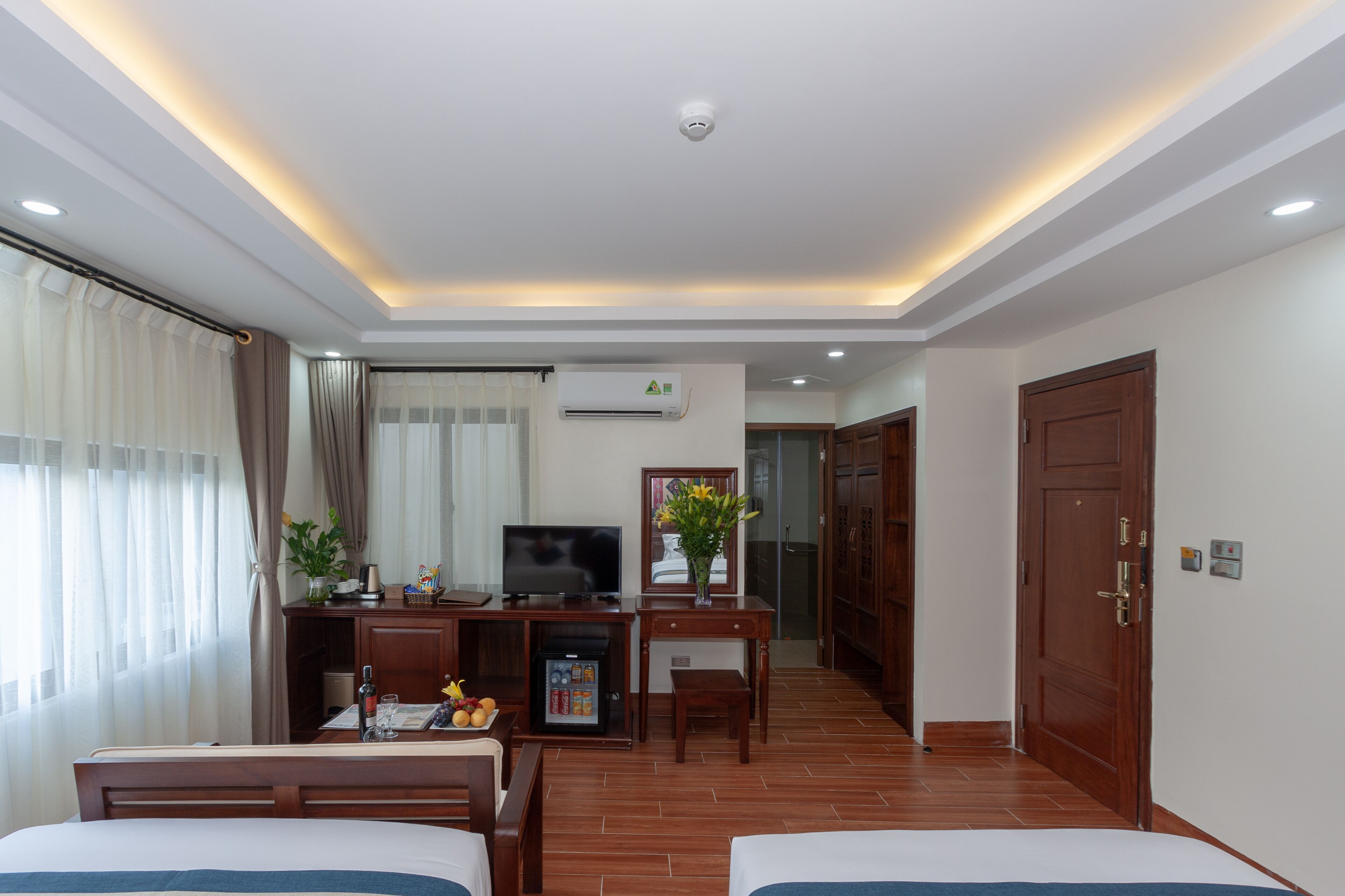A hotel room with a bed, a desk with a television, a minibar, and a view of the outside.