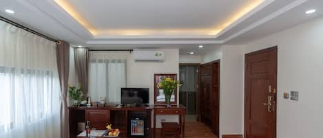 A hotel room with a bed, a desk with a television, a minibar, and a view of the outside.