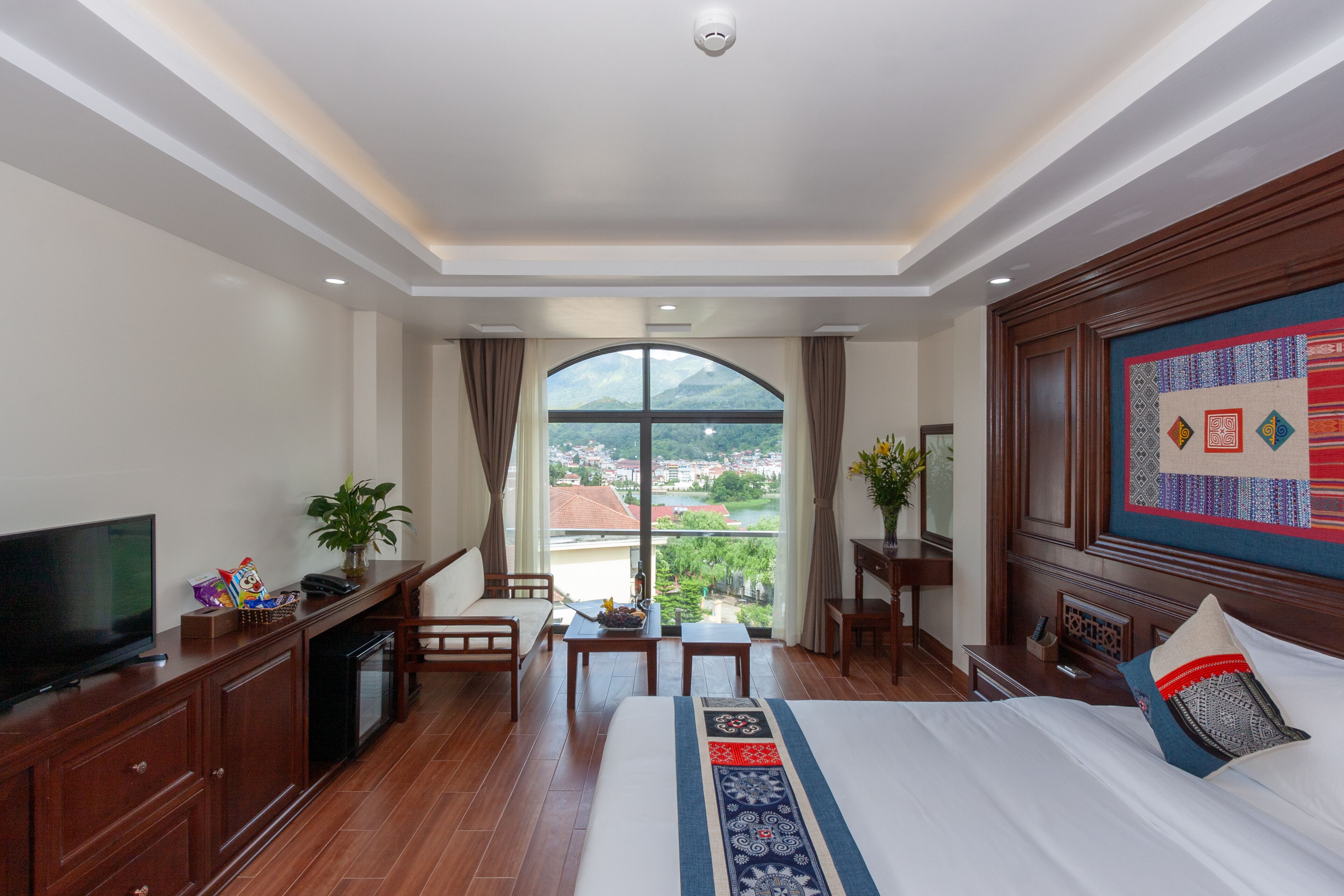 Une chambre d’hôtel avec un grand lit, une télévision, un bureau et une vue sur le paysage urbain, visible à travers une grande fenêtre.