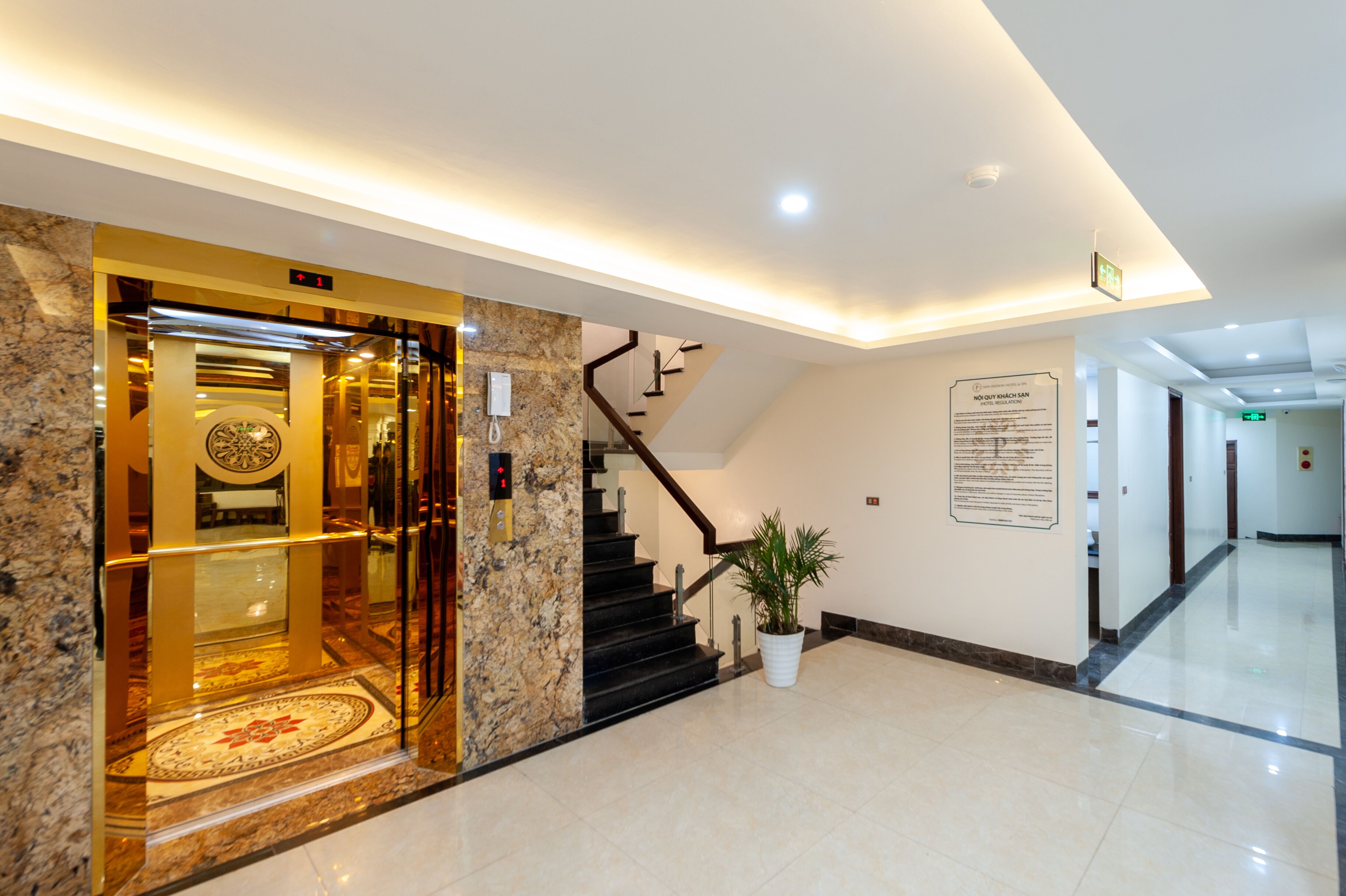 Un vestíbulo de hotel con una recepción de mármol, una escalera y una planta en maceta.
