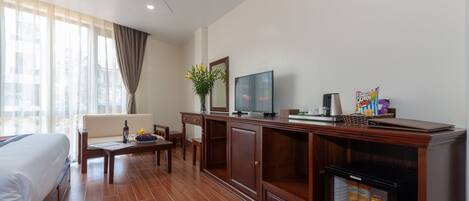 A hotel room with a bed, a sofa, a coffee table, a TV, a minibar, and a window with curtains.