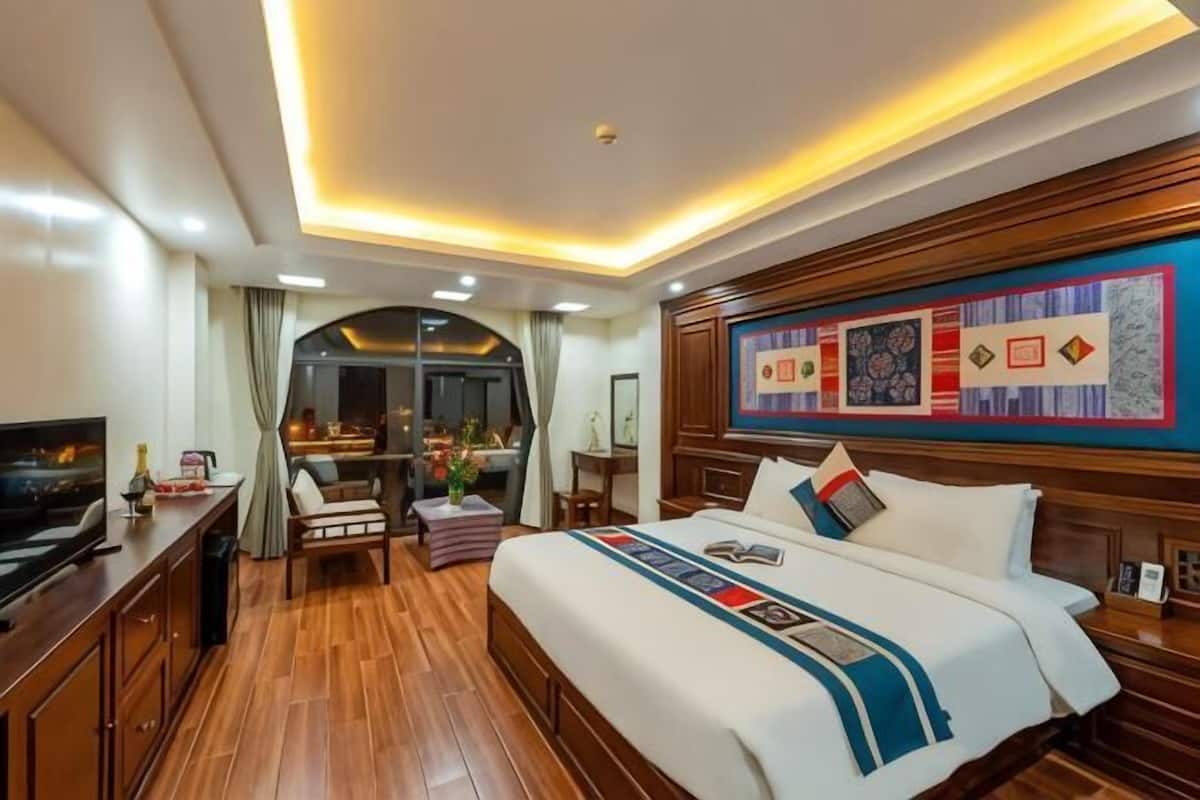 A hotel room with a large bed, wooden flooring, a television, a desk, and a view of the outside.
