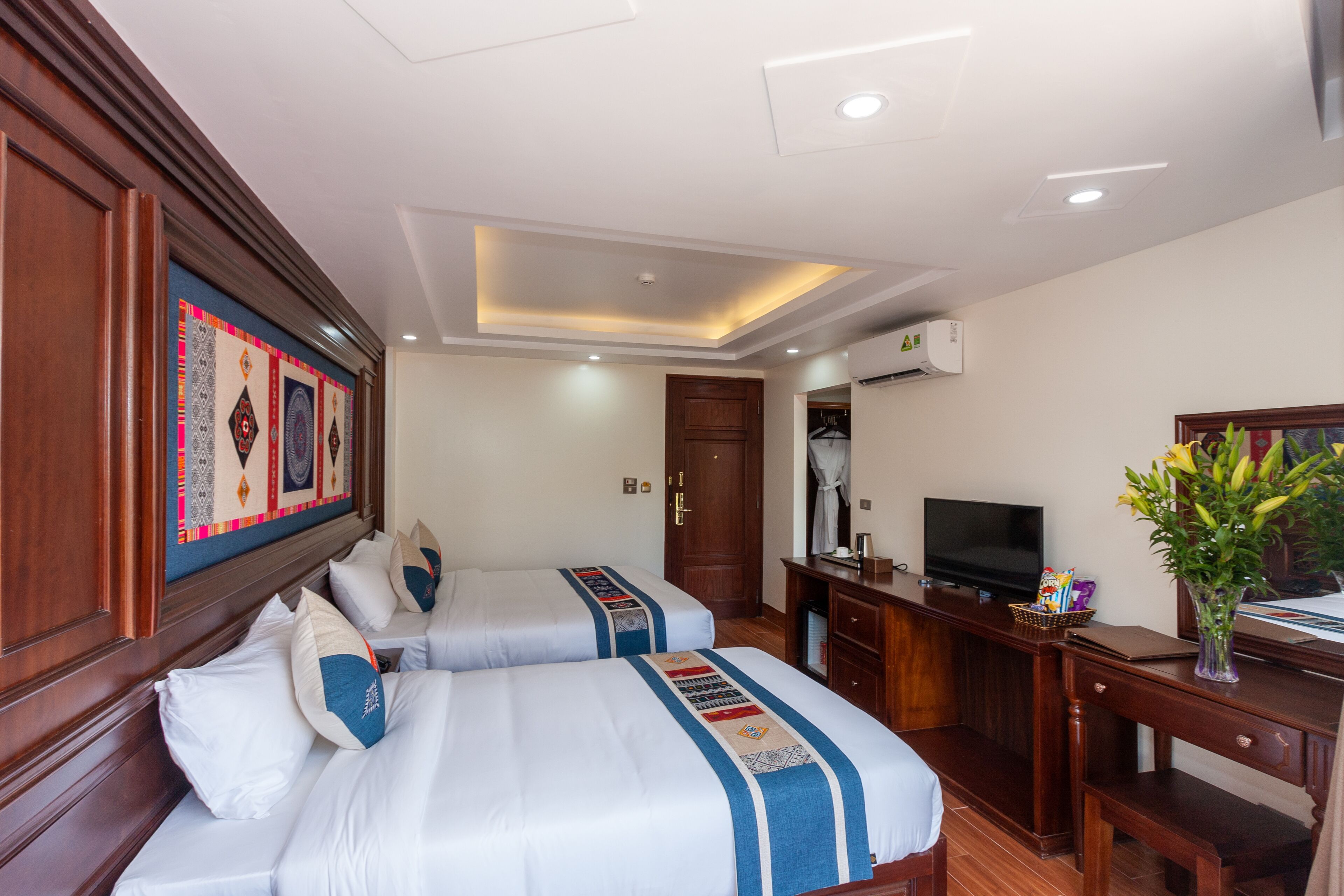 A hotel room with two beds, a desk, a television, and a decorative wall hanging.