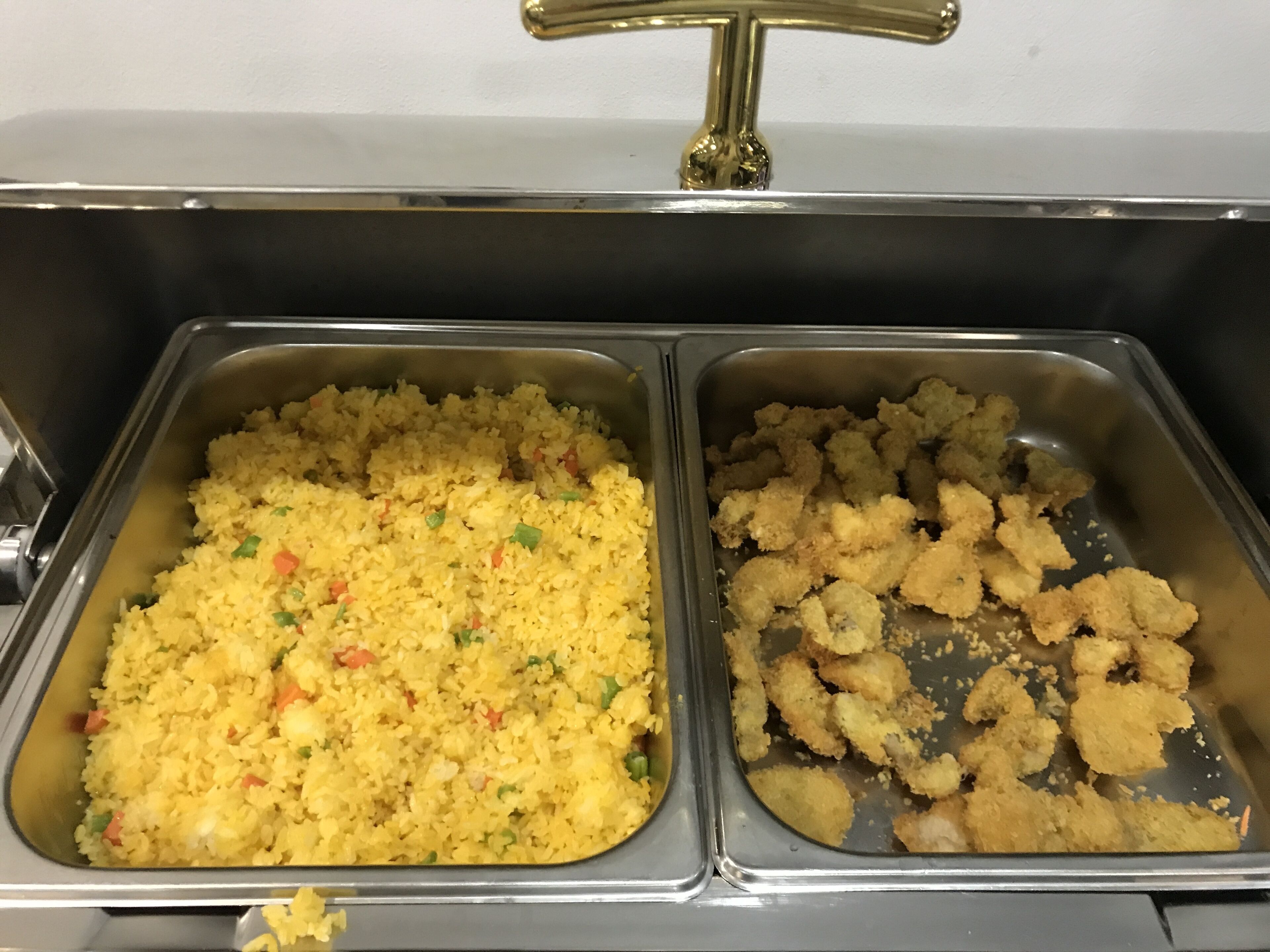 A buffet with two trays of food: one with yellow rice and vegetables, and another with breaded chicken pieces.