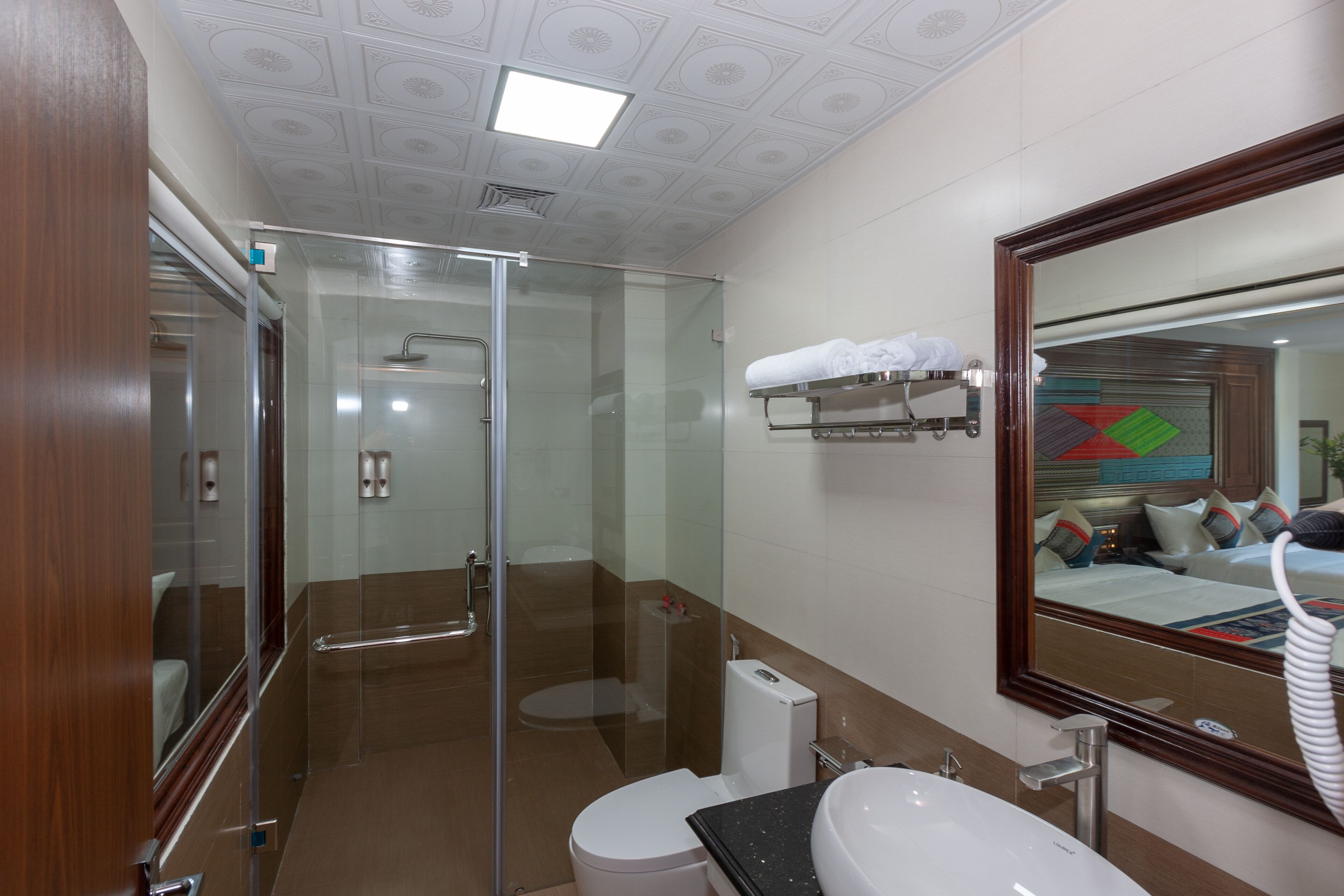 Un baño moderno con cabina de ducha de vidrio, inodoro blanco, lavamanos con encimera negra y espejo con marco de madera.