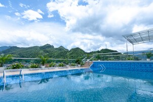 Piscina con vistas a montañas, zona cubierta y plantas en macetas.