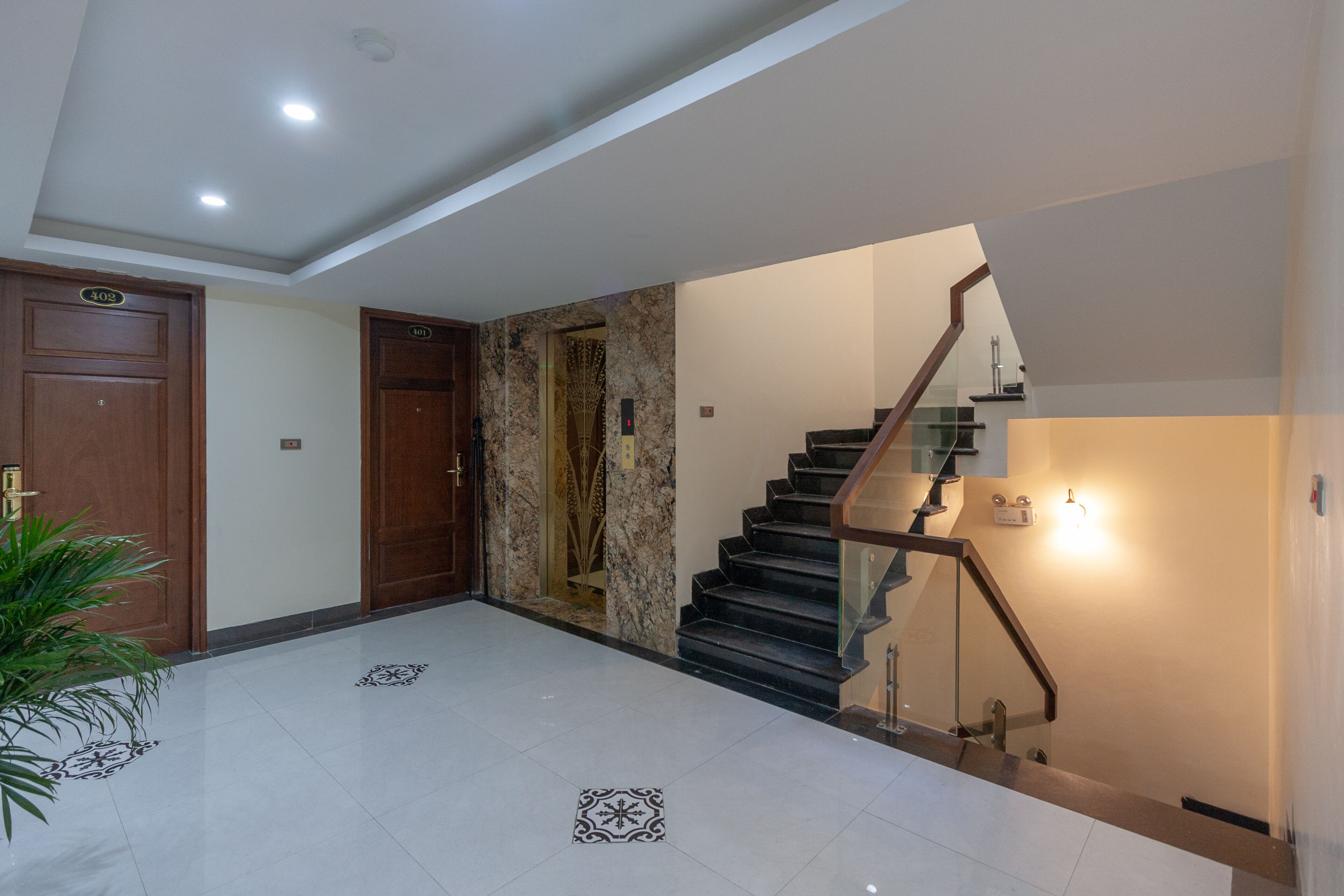 A modern interior with a marble wall, a staircase with glass railings, and a potted plant.