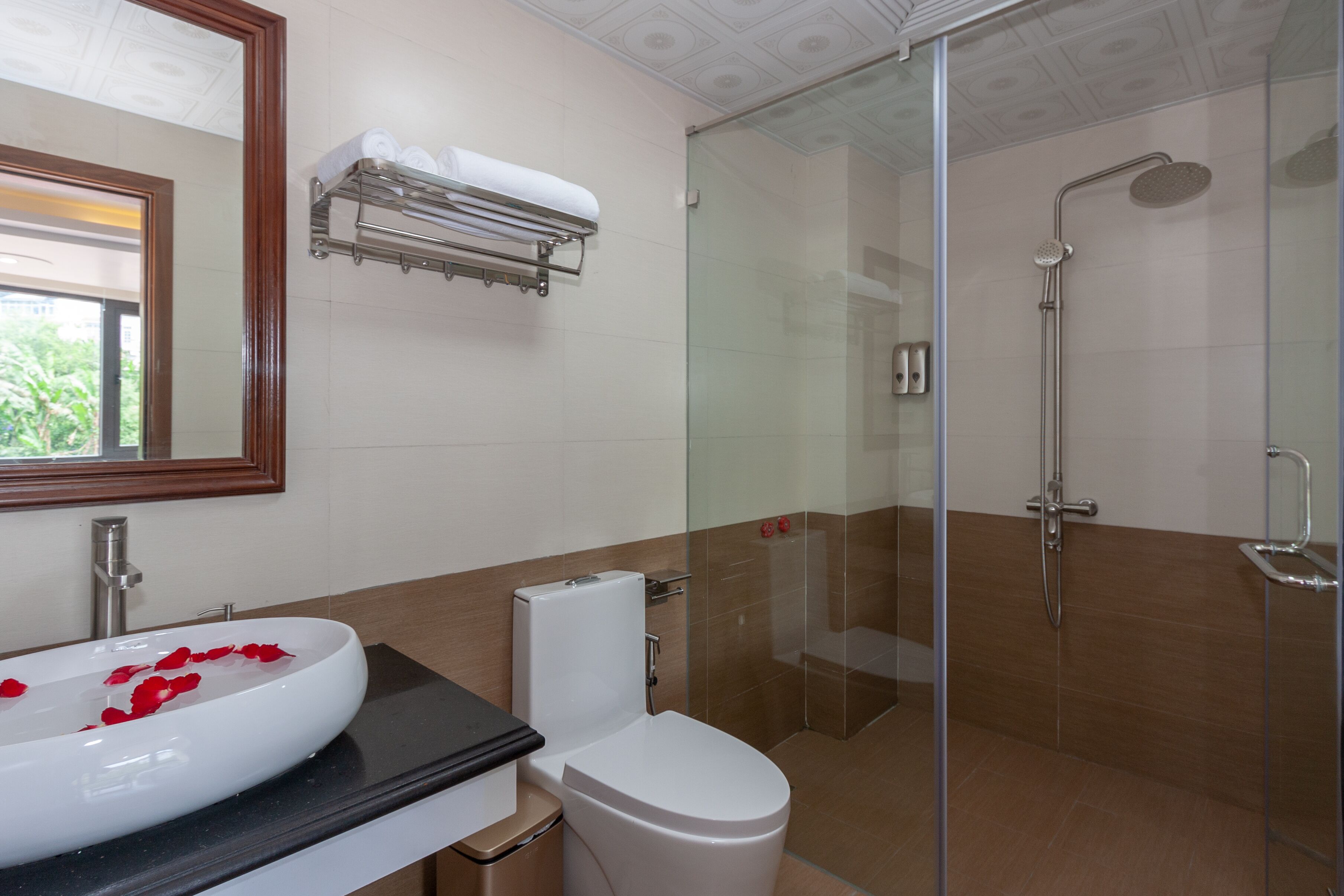 A modern bathroom with a glass-enclosed shower, a white sink with rose petals, a toilet, and a towel rack.