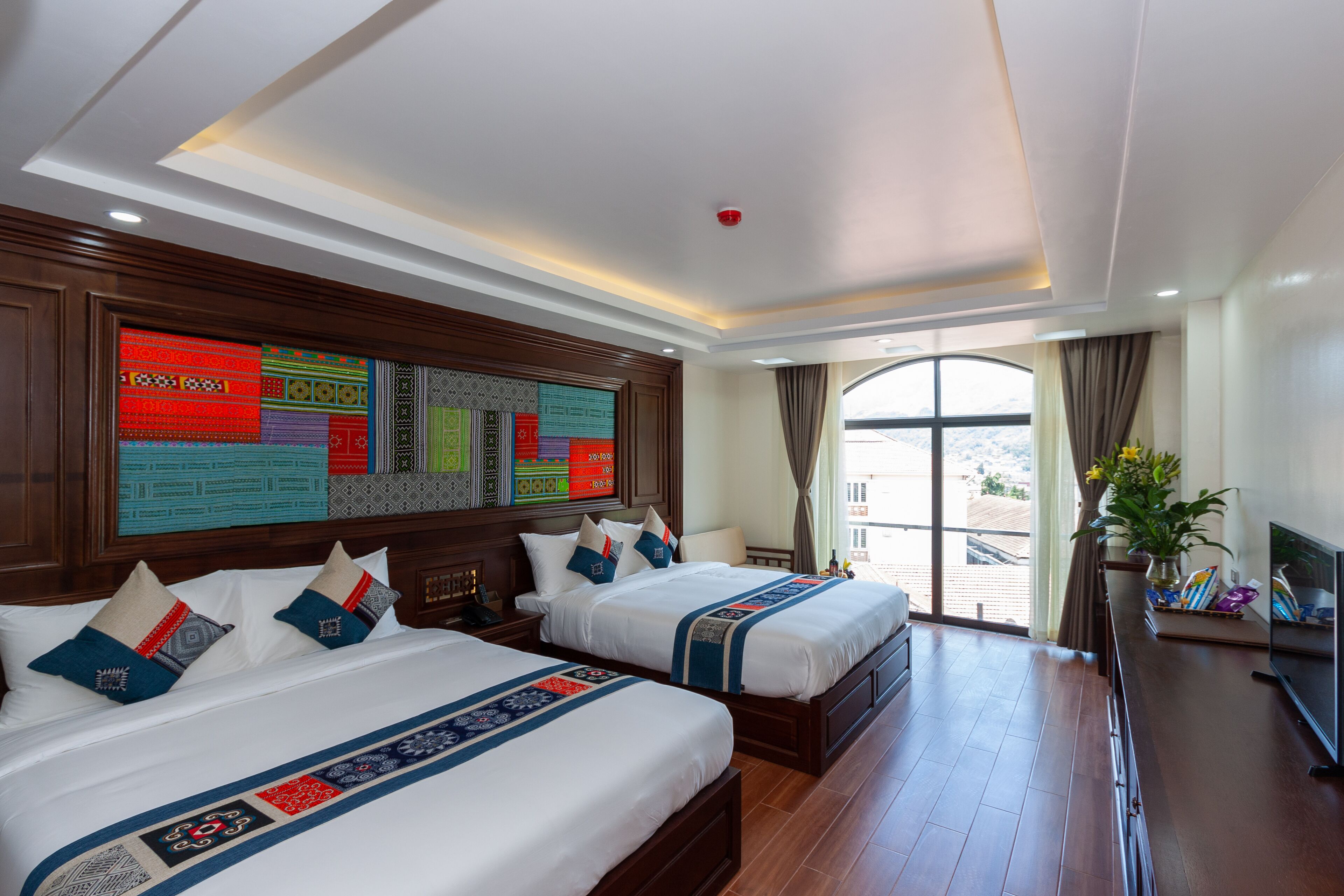 A hotel room with two beds, a large window, a TV, and a decorative wall panel.