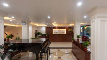 Un vestíbulo de hotel con un piano de cola, una recepción y plantas en macetas.
