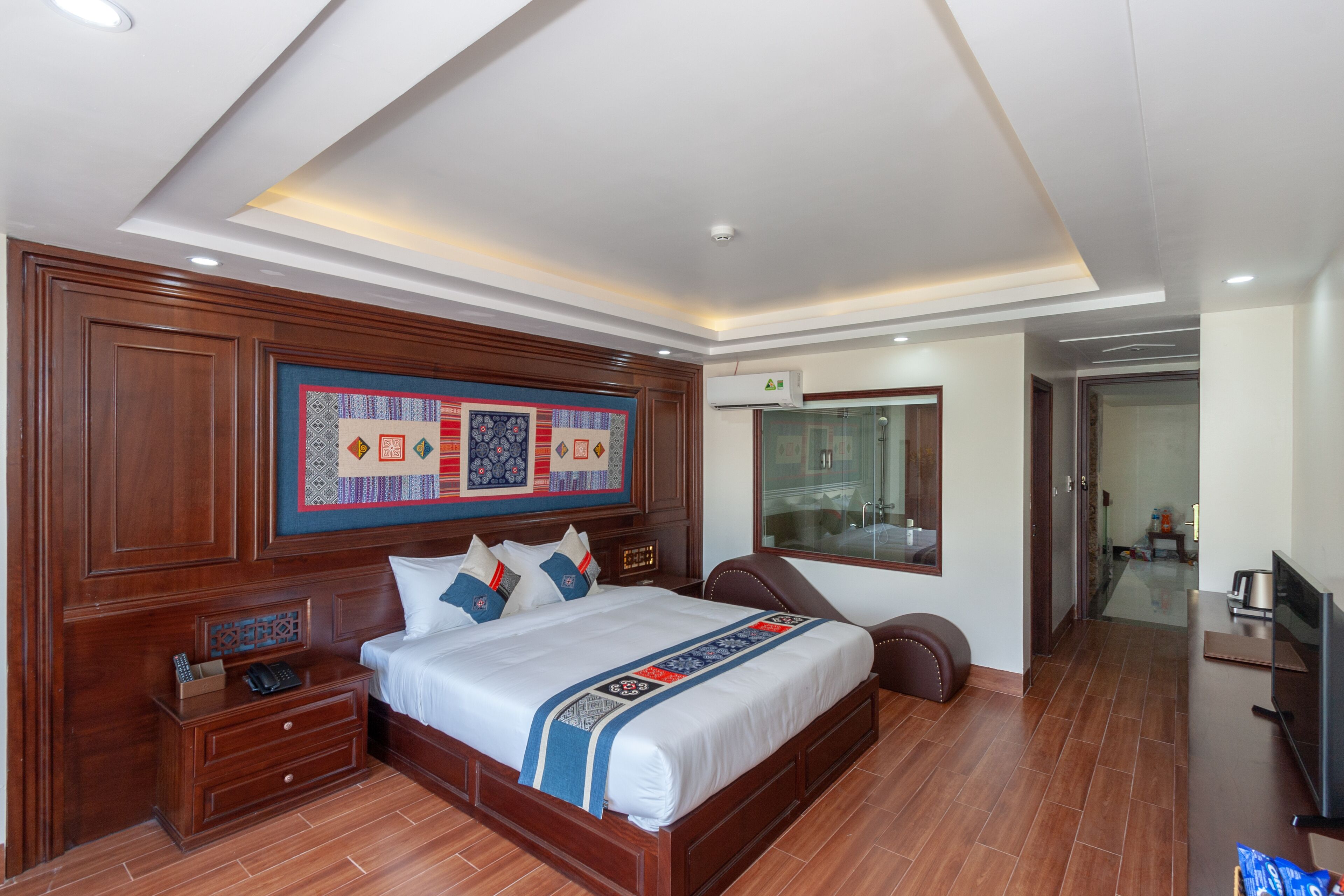 A modern hotel room with a large bed, wooden headboard, a flat-screen TV, and a large window.