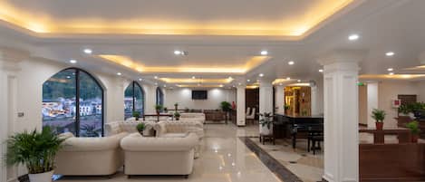 A spacious lobby with a piano, sofas, and potted plants.
