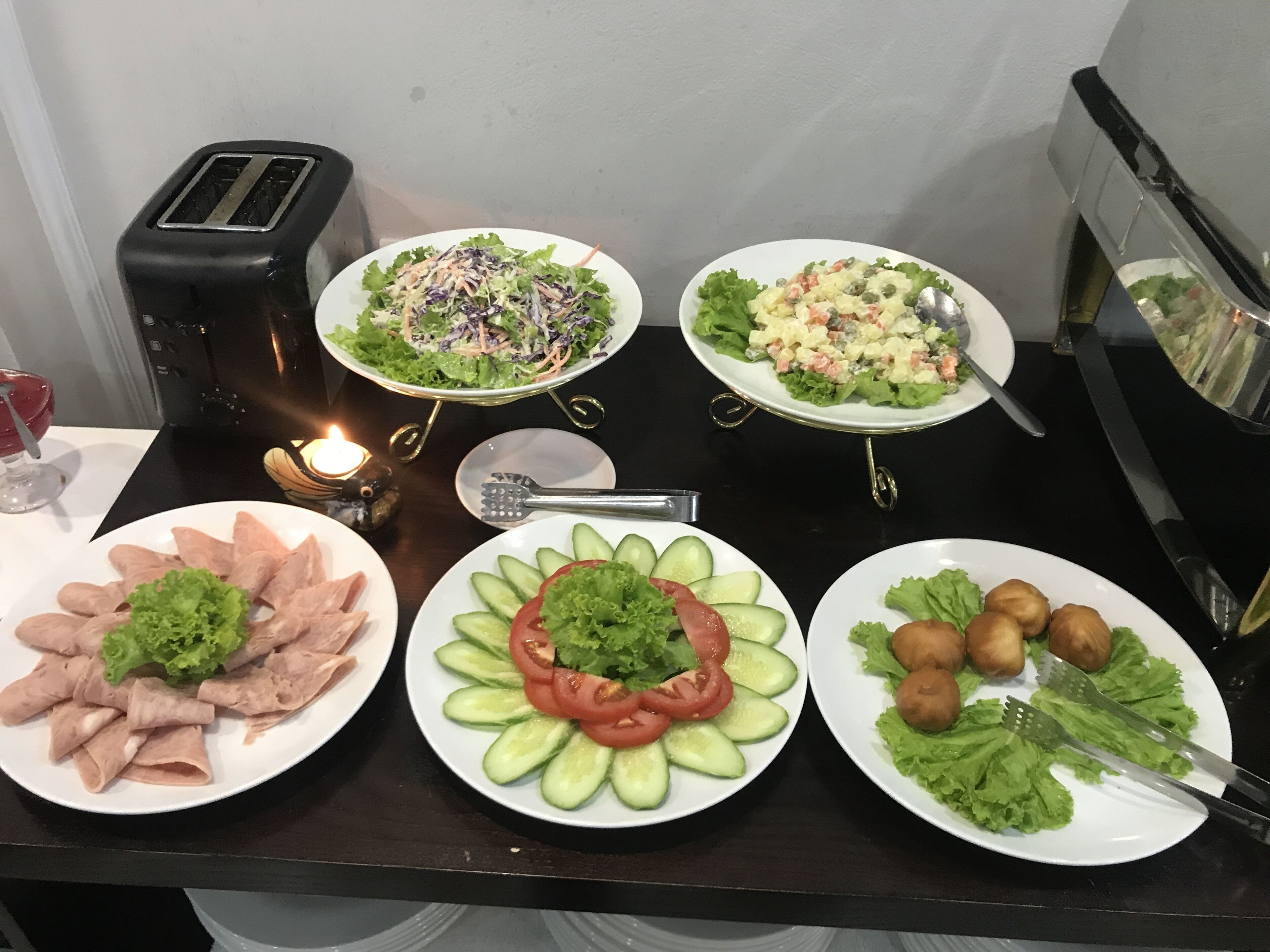 A dining table with various plates of food, a toaster, and a candle.