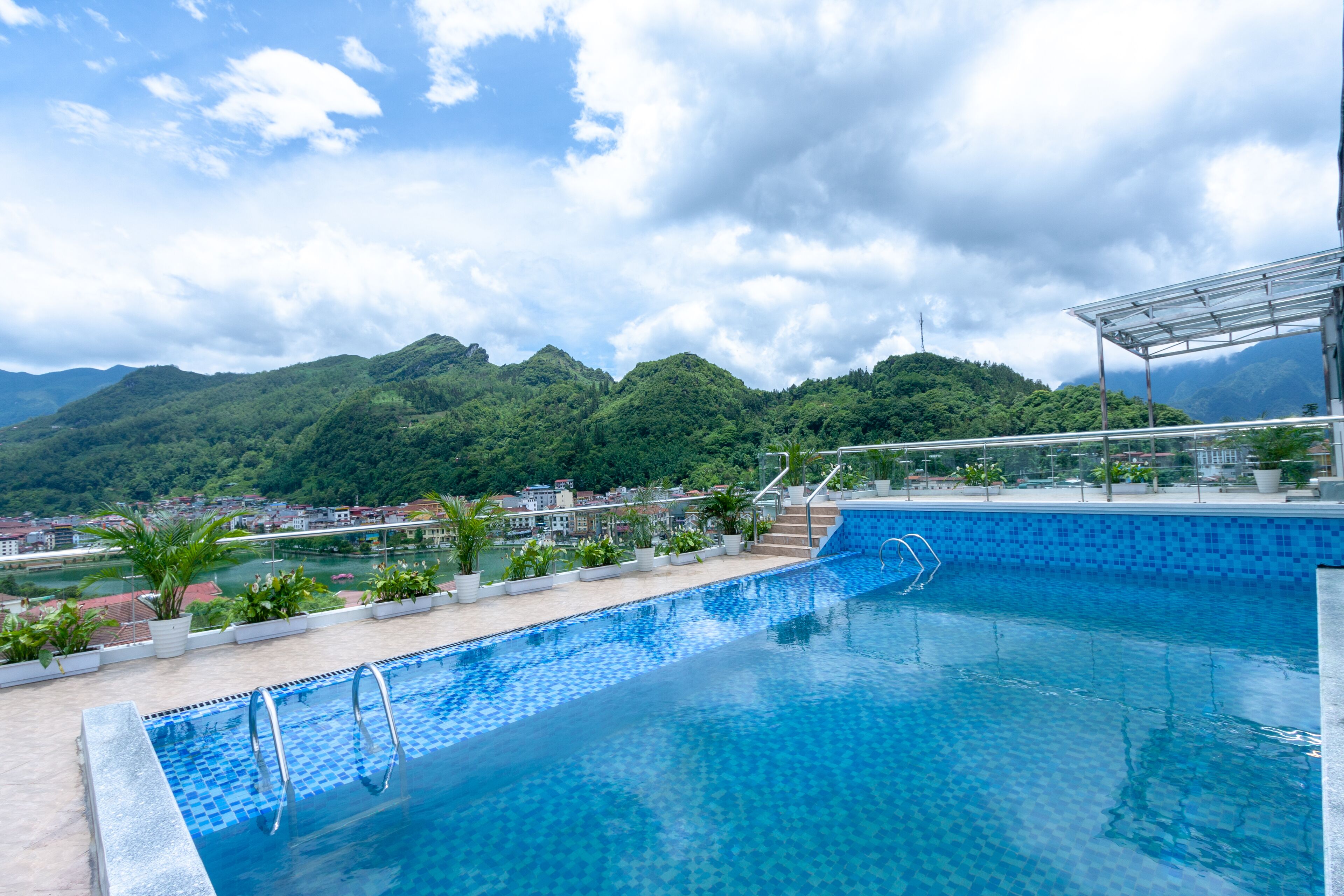 A swimming pool with clear blue water, surrounded by potted plants and a view of mountains in the background.