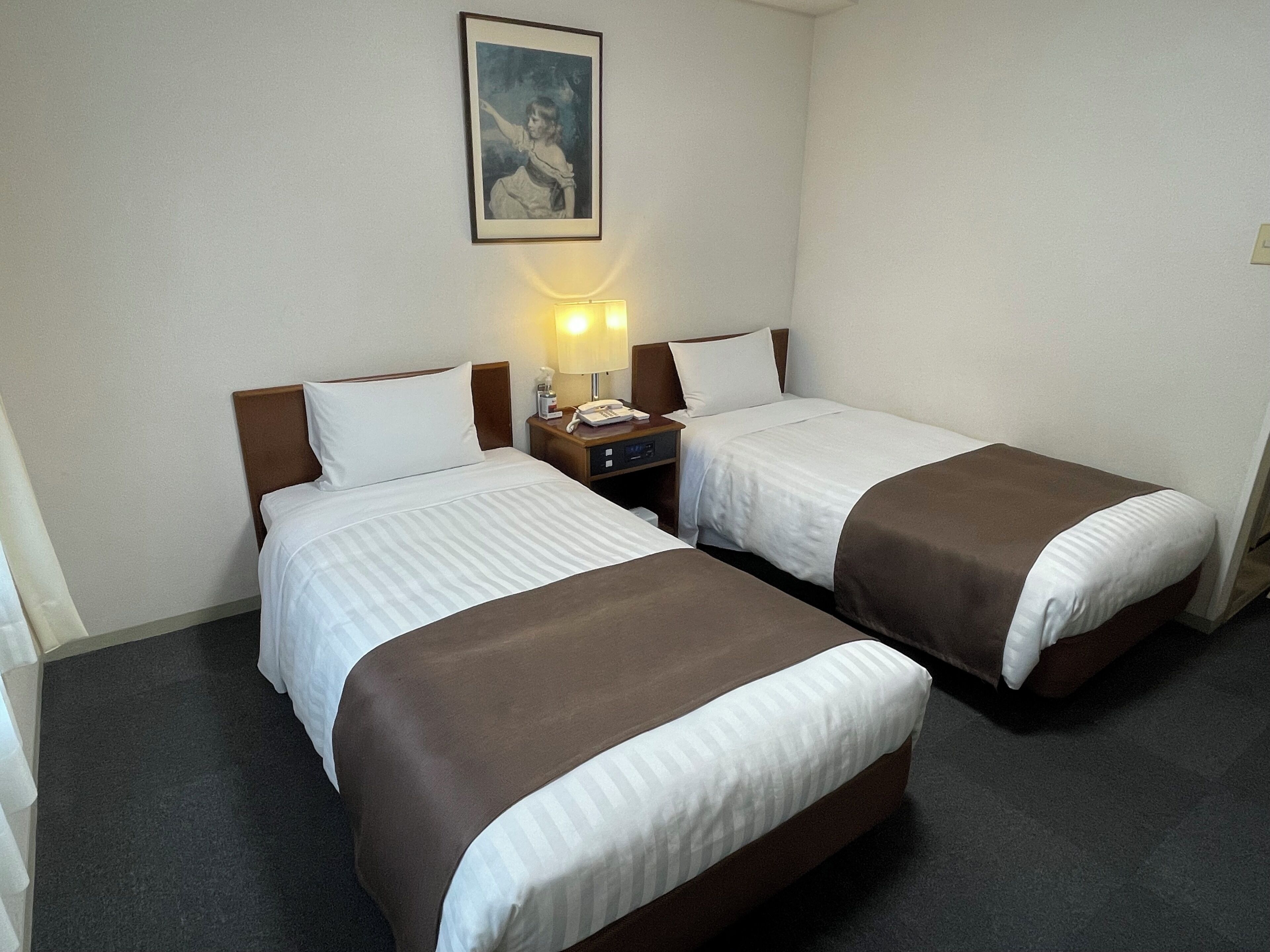 A hotel room with two beds, a nightstand with a lamp, and a framed picture on the wall.