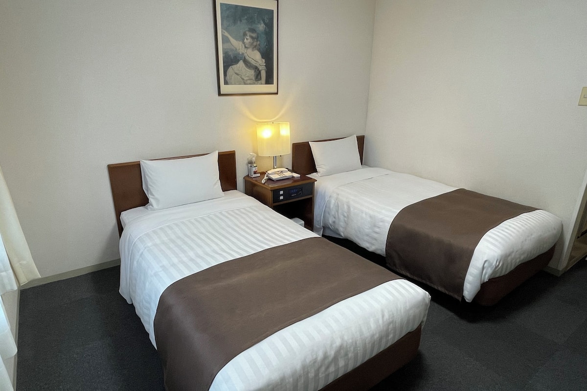 A hotel room with two beds, a nightstand with a lamp, and a framed picture on the wall.