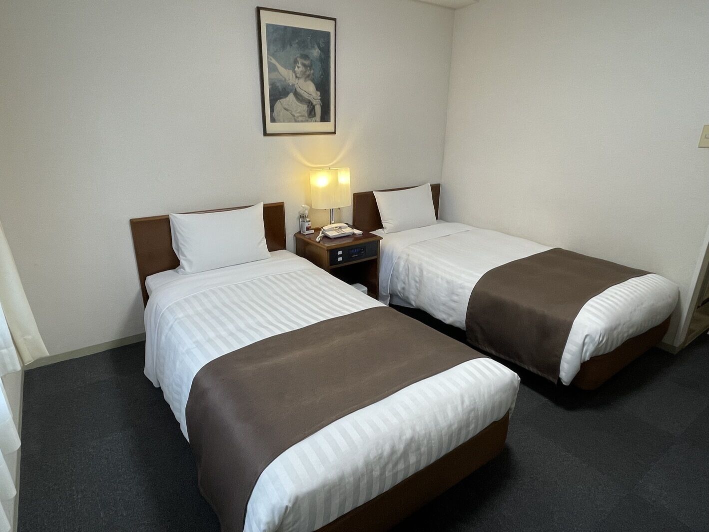 A hotel room with two beds, each with a brown bedspread, a nightstand with a lamp, and a framed picture on the wall.