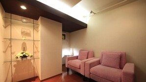 A room with a glass display unit, two pink sofas, a wooden floor, and a ceiling light. - Shinjuku Urban Hotel (Tokyo)