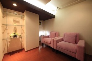 A room with a glass display unit, two pink sofas, a wooden floor, and a ceiling light.