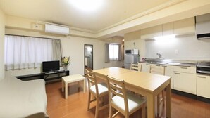 A compact hotel room with a bed, a small desk, a television, a dining table with chairs, a kitchenette, and a bathroom. - Shinjuku Urban Hotel (Tokyo)