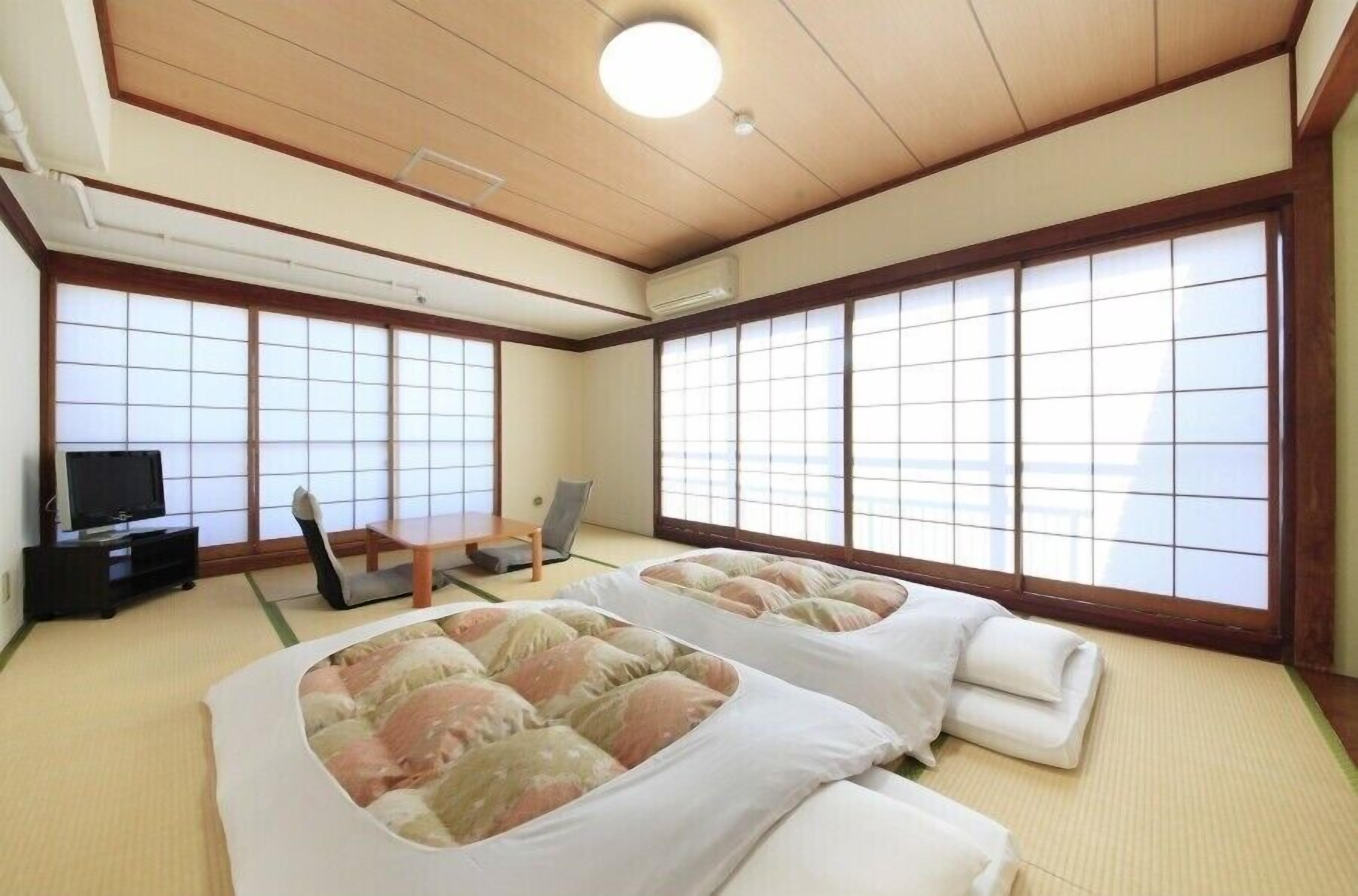 A traditional Japanese-style room with tatami flooring, two tatami beds, a television, and sliding doors.