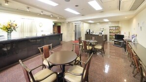 A reception area with a counter, chairs, tables, a television, and a plant. - Shinjuku Urban Hotel (Tokyo)