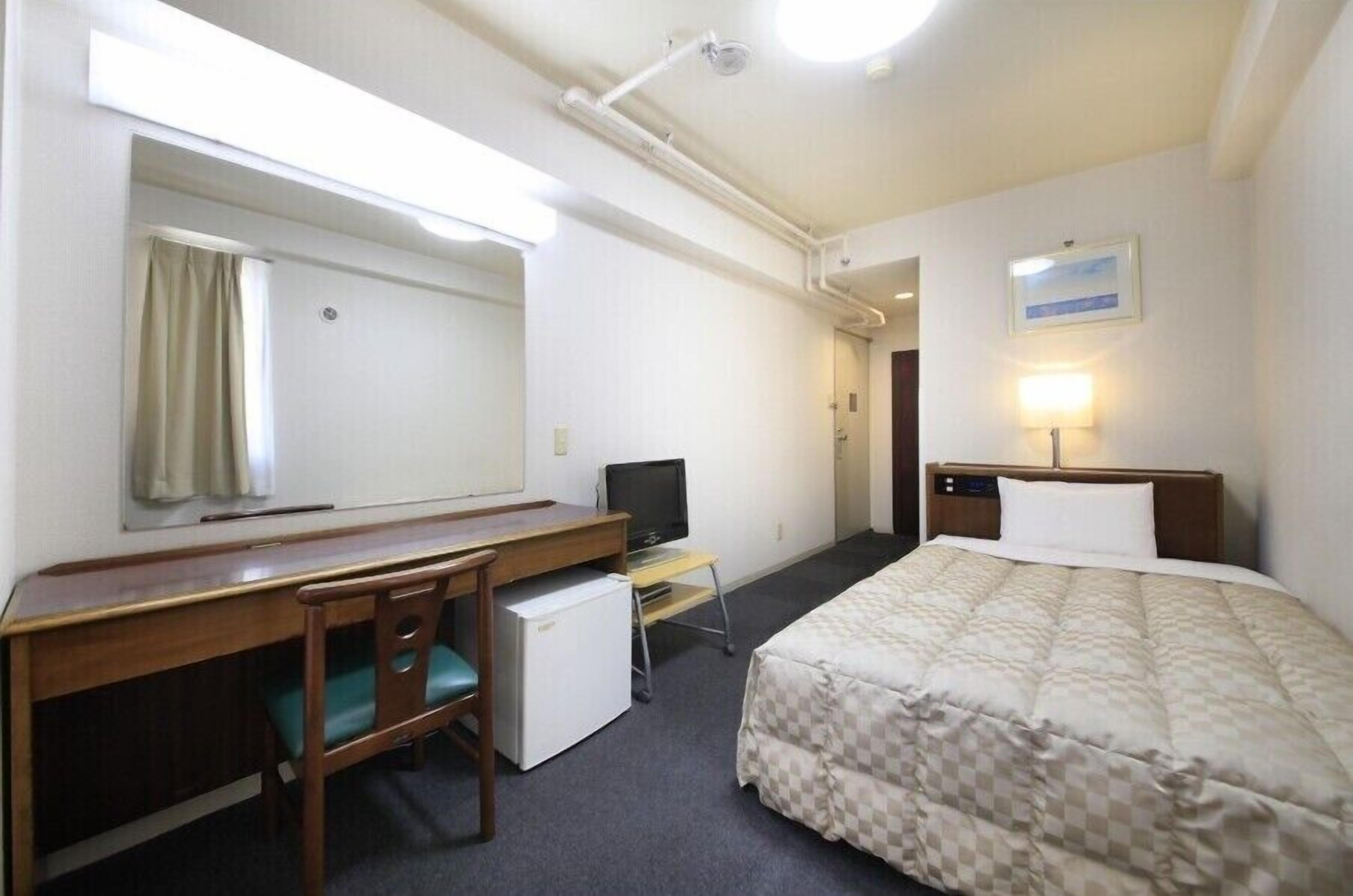 A hotel room with a bed, desk, chair, television, and a mirror.