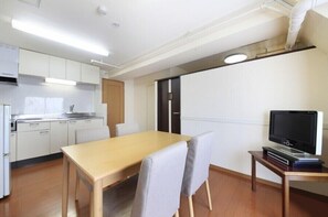 A compact kitchen with white cabinets, a wooden dining table, and a television on a small stand.